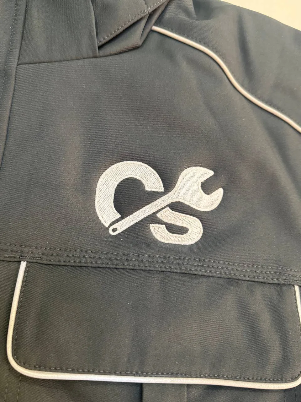 Dunkle Arbeitsjacke mit weiß gesticktem Monogramm-Logo auf der Brust