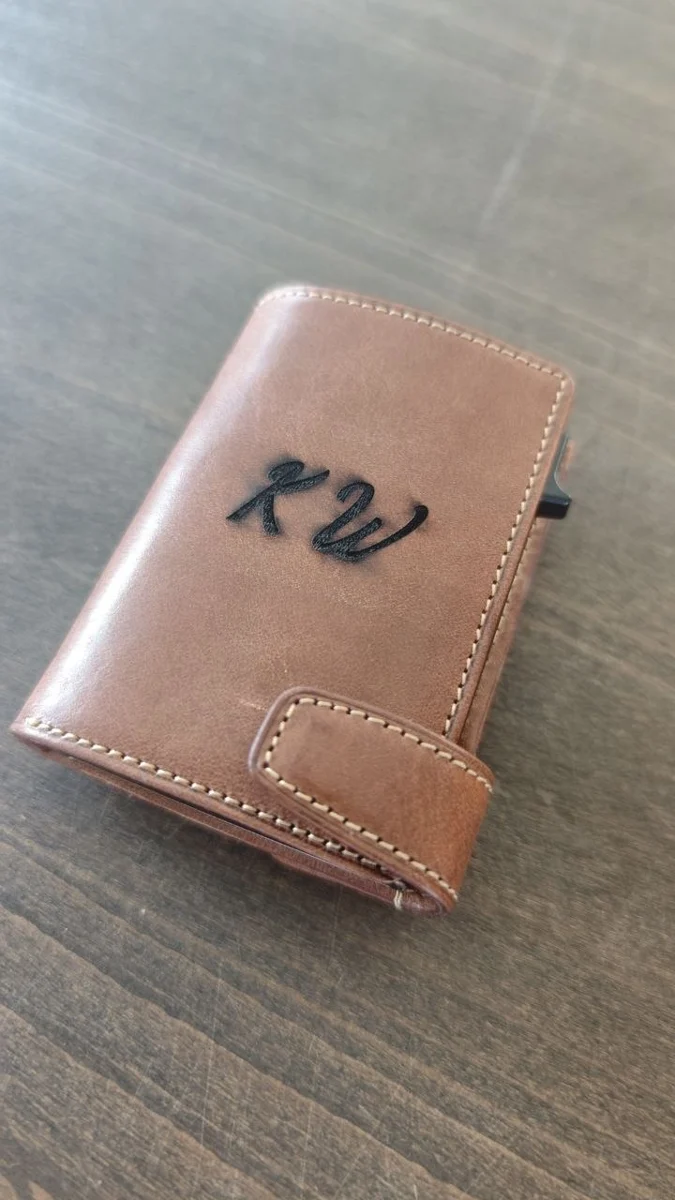Braunes Lederetui mit dunkel graviertem Monogramm auf einer Holzoberfläche