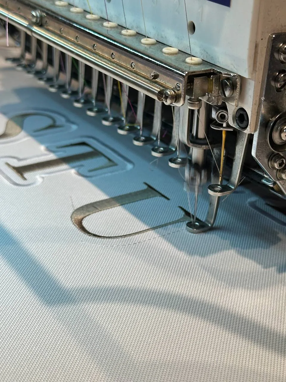Mehrkopf-Stickmaschine stickt ein Logo auf helles Textil, Produktion in Wien 1220