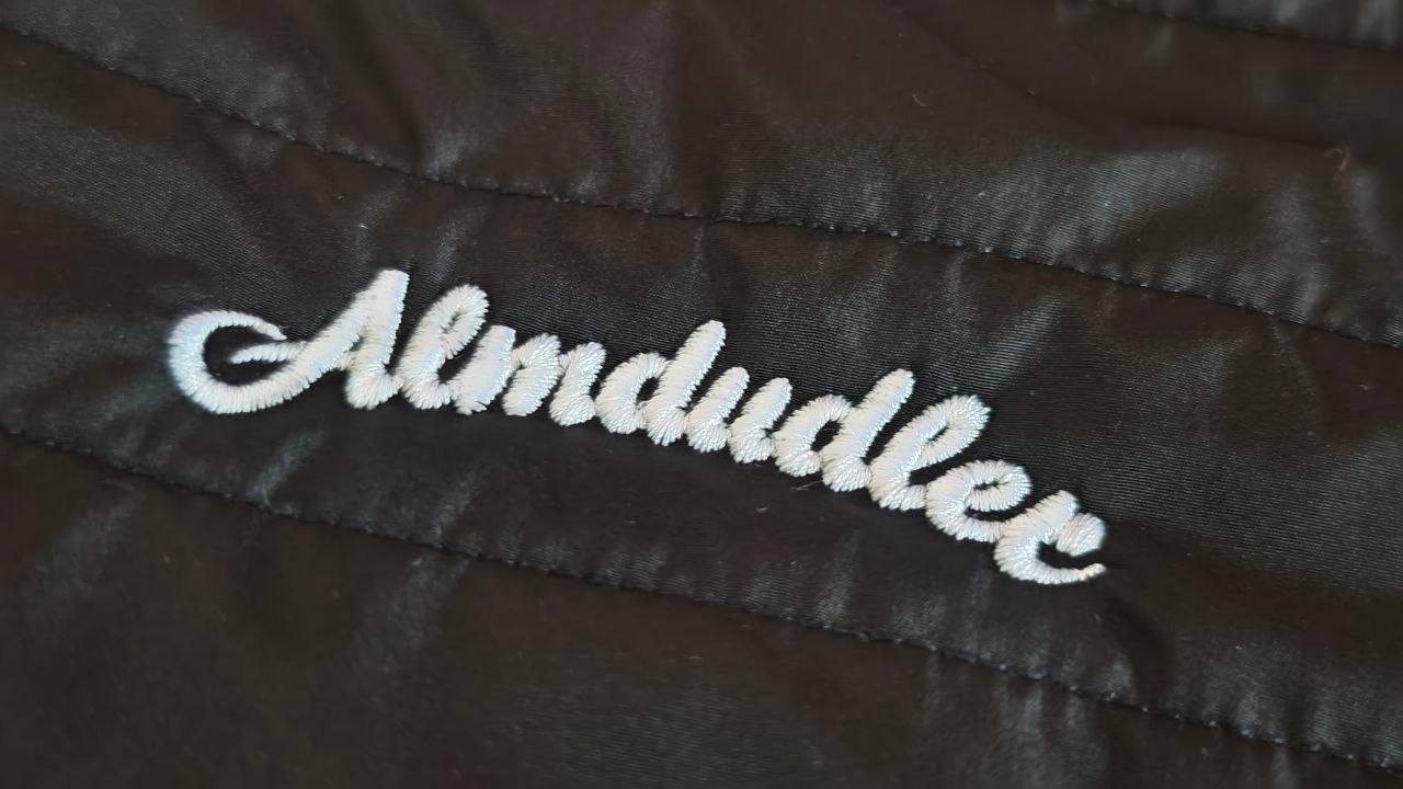 Weiß gestickter Markenschriftzug auf dunkler Steppjacke, Logostickerei Wien