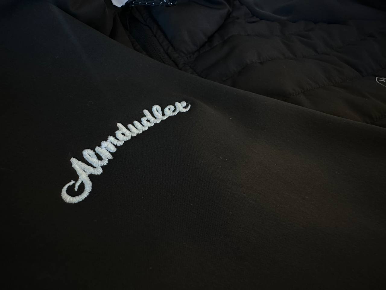 Weiß gestickter Schriftzug auf schwarzer Jacke, Detailaufnahme der Stickerei