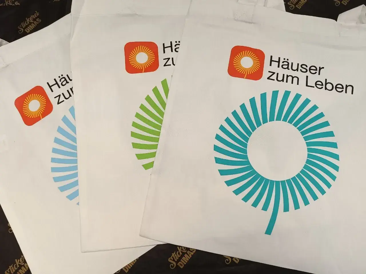 Drei weiße Baumwolltaschen mit mehrfarbigem Siebdruck Logo