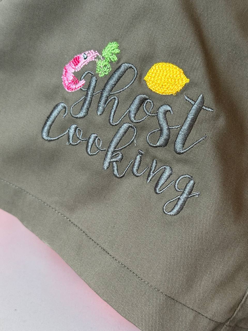 Gestickter Schriftzug auf olivgrüner Arbeitsjacke, Detailaufnahme