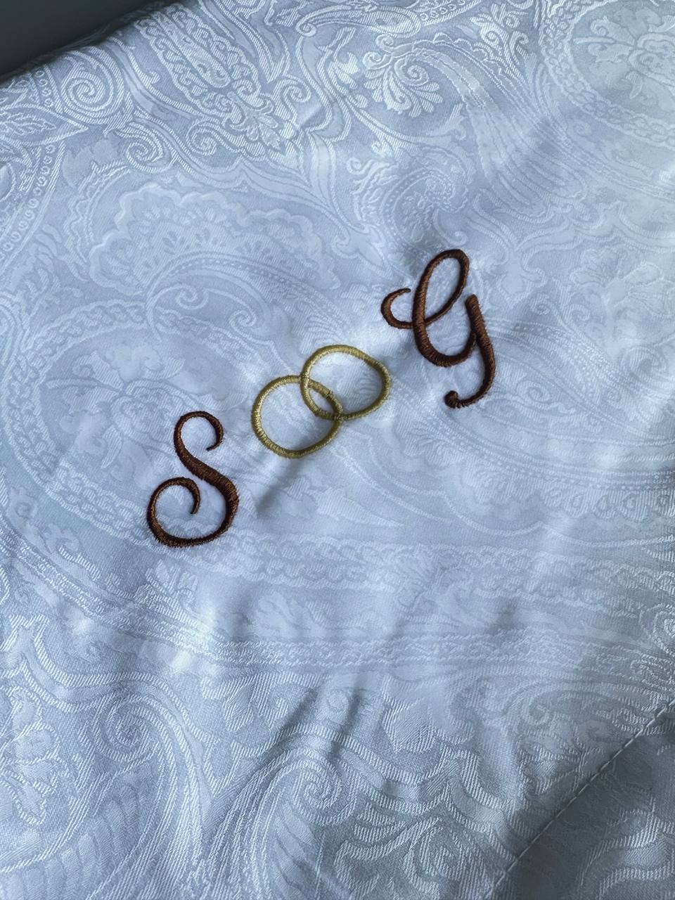 Nahaufnahme eines gestickten Monogramms in Braun und Gold auf weißem Stoff