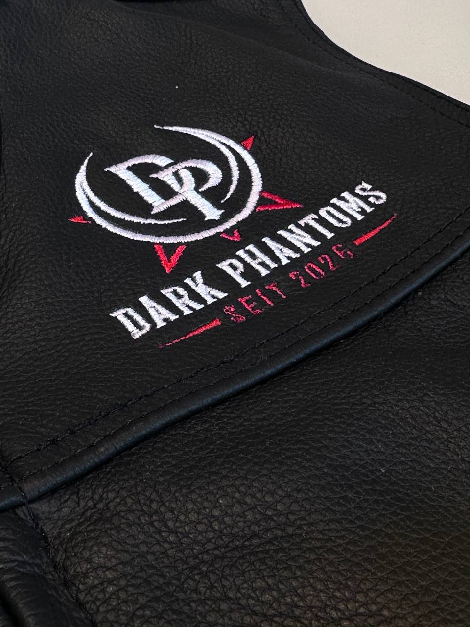 Detailaufnahme eines gestickten Logos am Kragen einer schwarzen Jacke