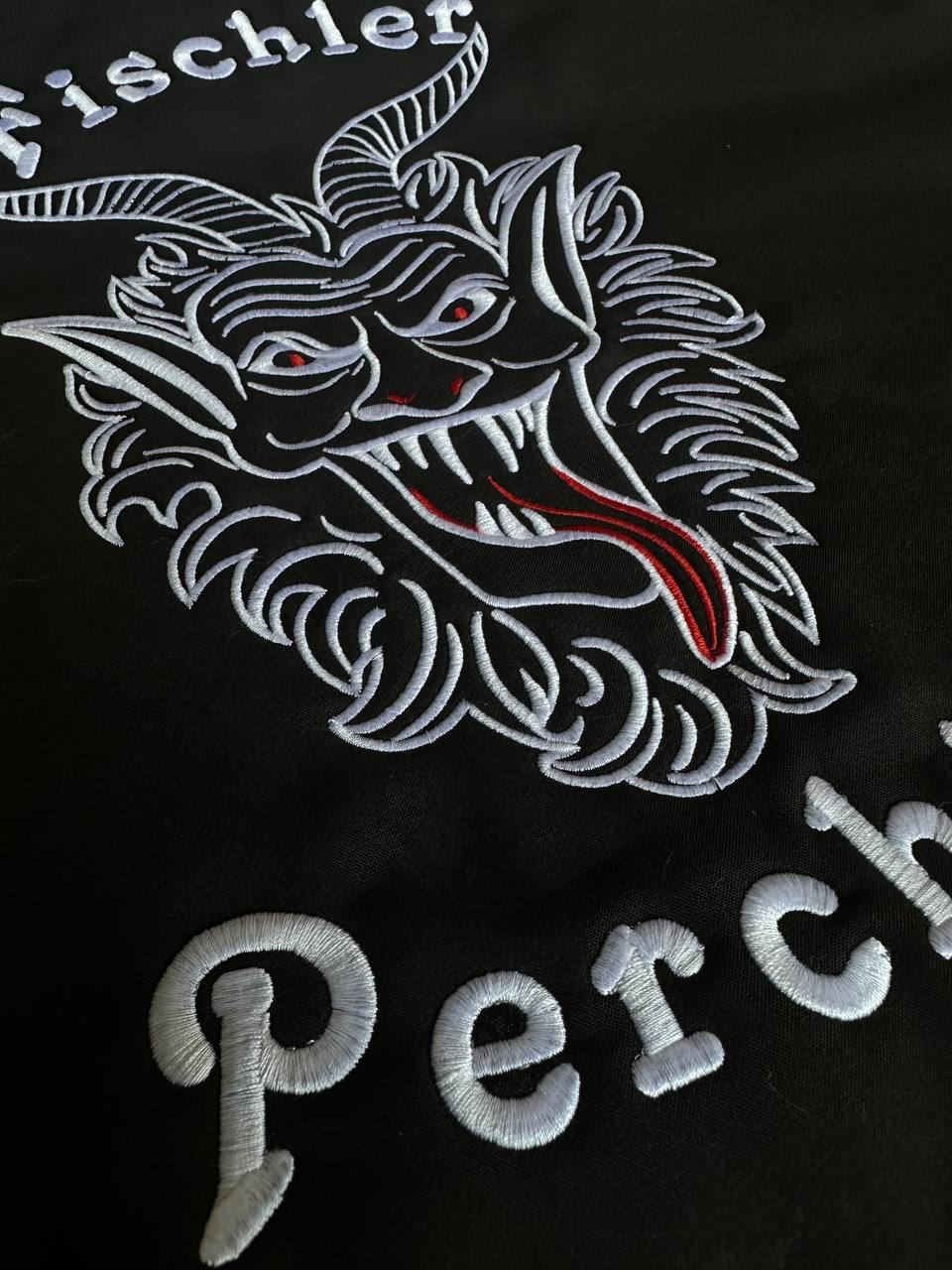 Detailaufnahme einer weißen Perchtenstickerei auf schwarzem Textil