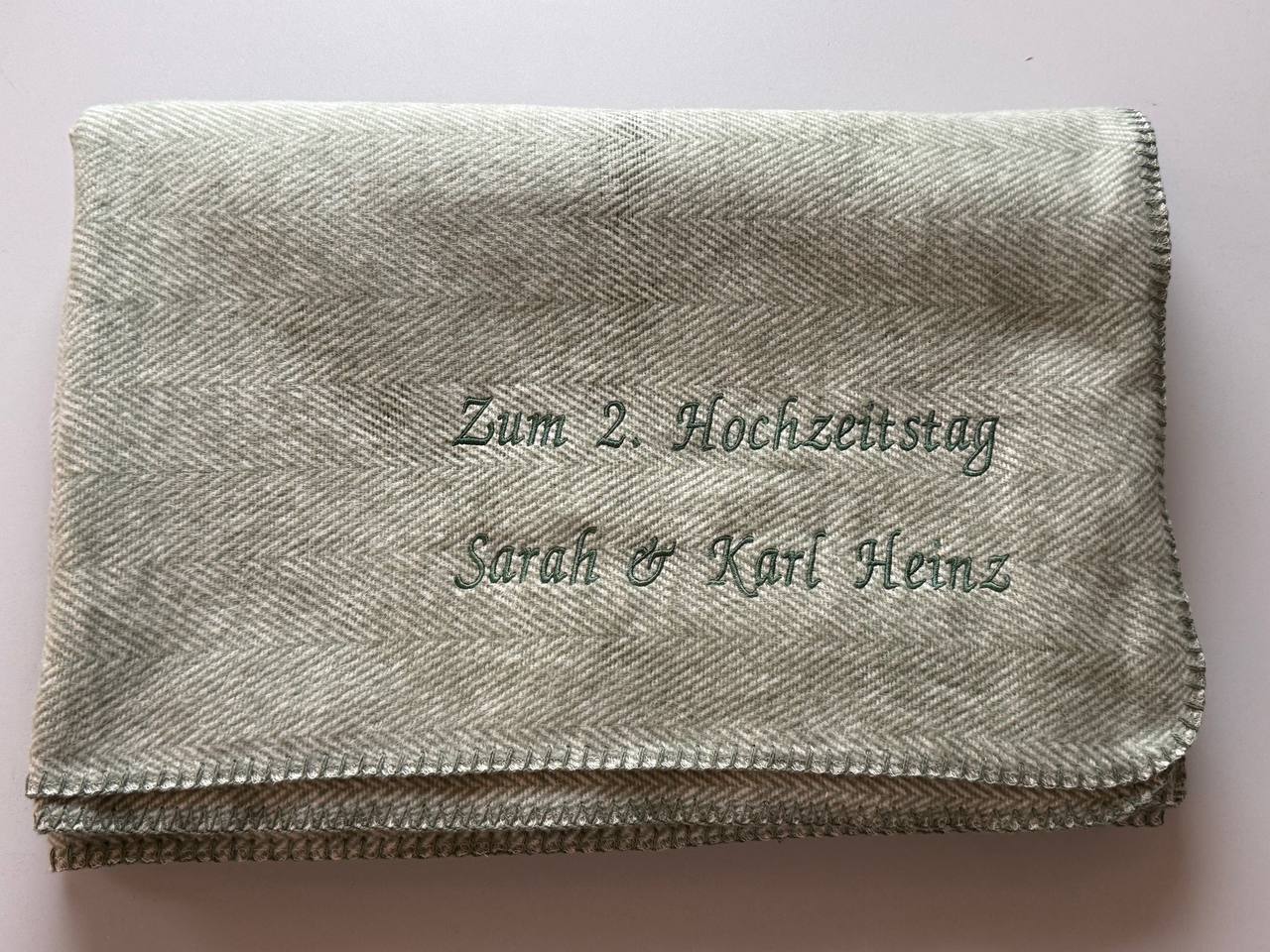 Graues Textil mit persönlicher Schriftstickerei, zusammengelegt fotografiert