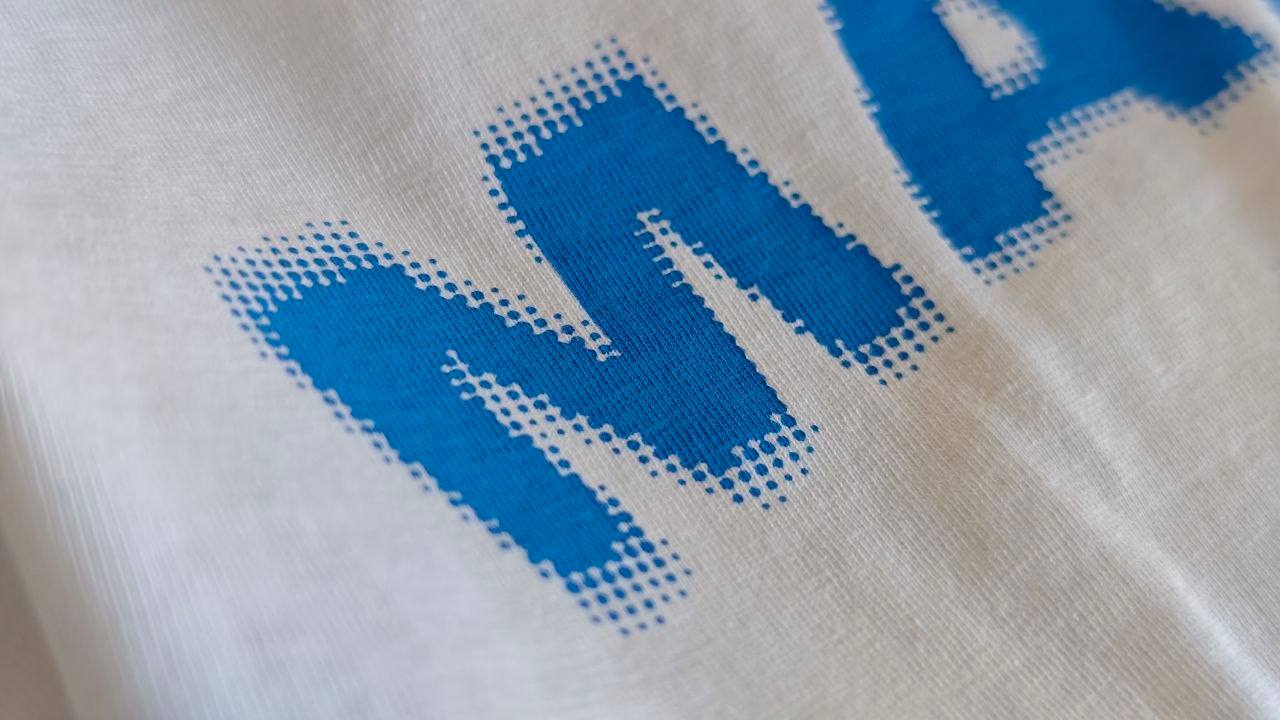 Detailaufnahme eines blauen Schriftdrucks in Pixeloptik auf weißem Shirt