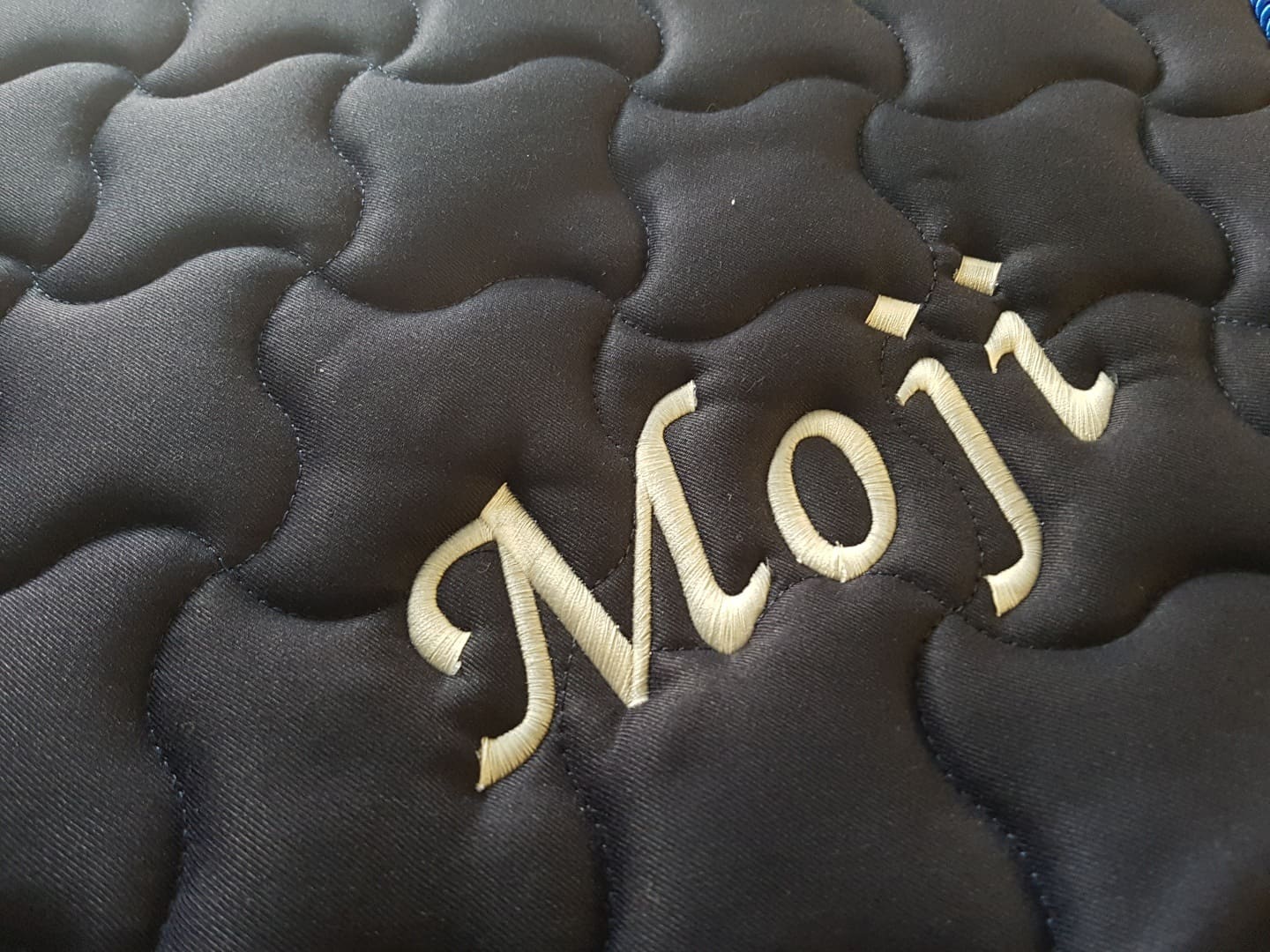Detailaufnahme Stickerei Moji auf Satteldecke, goldene Schreibschrift auf schwarzem Stoff