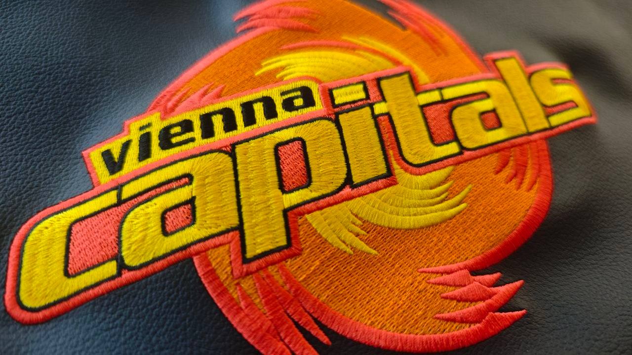 Mehrfarbiges Vereinslogo in Gelb und Orange auf dunklem Textil gestickt
